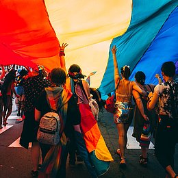 Menschen laufen unter einer Regenbogenflagge ©Mercedes Mehling / unsplash.com