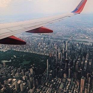 Blick aus dem Flugzeug auf eine Tragfläche, darunter befindet sich die Skyline New Yorks mit dem Central Park ©Natalie Dupin / pexels.com